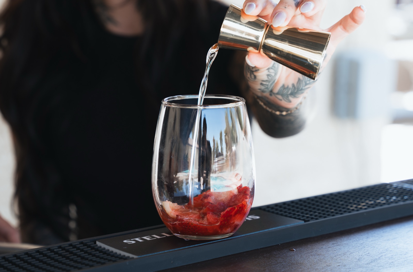 Gold jigger pouring a measure into a glass of muddled strawberries